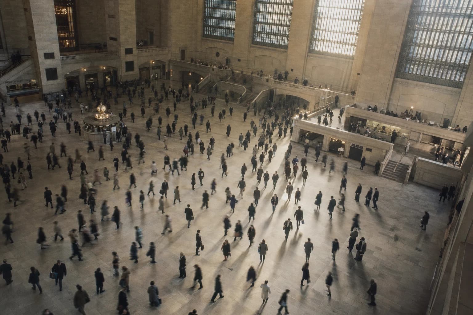 Commuters crossing a monumental New York rail concourse in the morning light.
