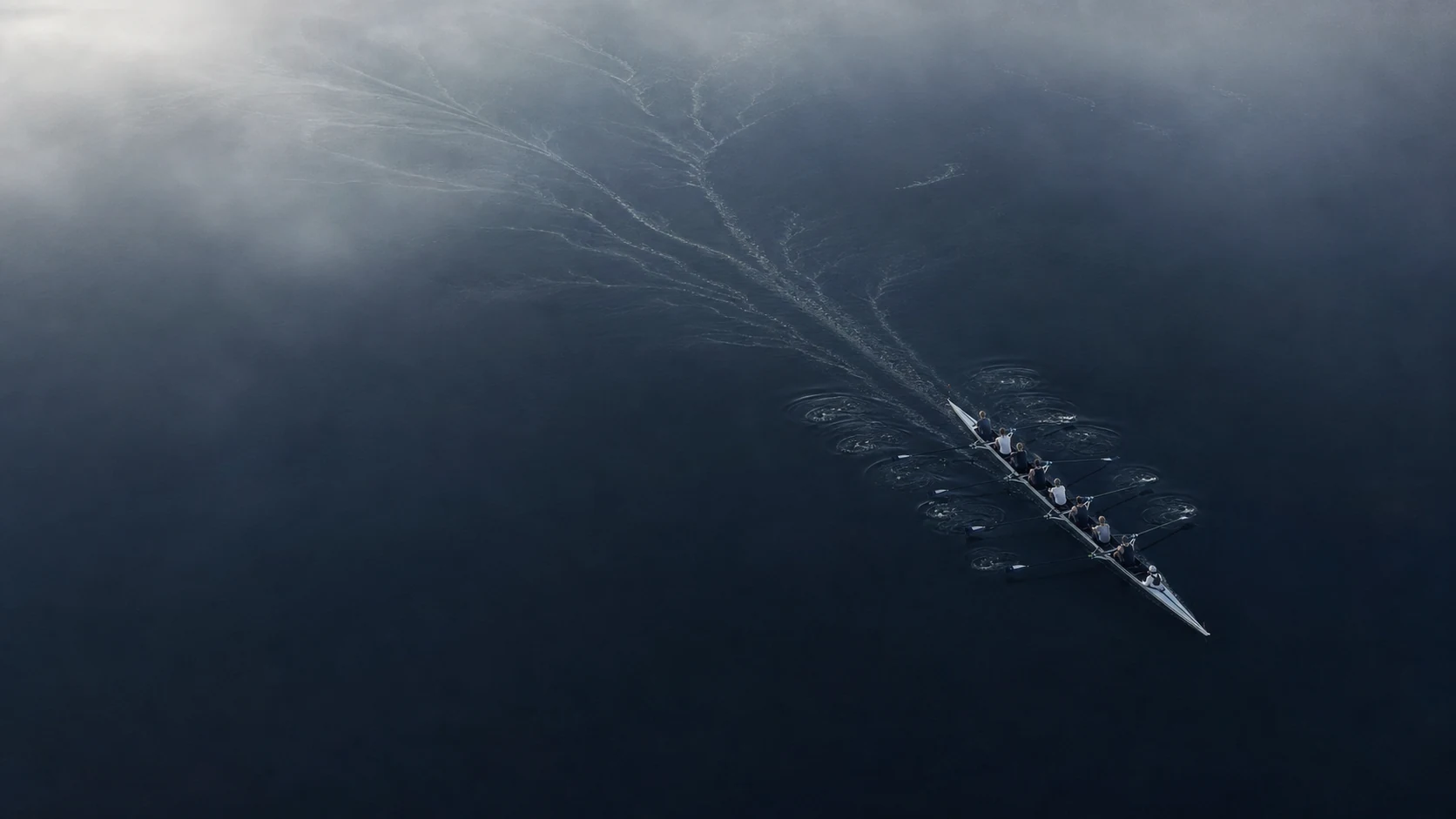 An eight-person rowing crew moving together across blue-black water.
